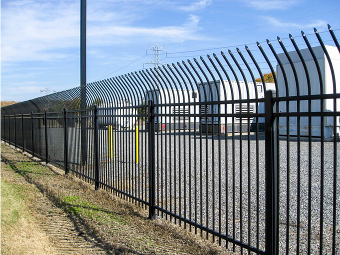 A black-steel commercial fence surrounding an industrial facility