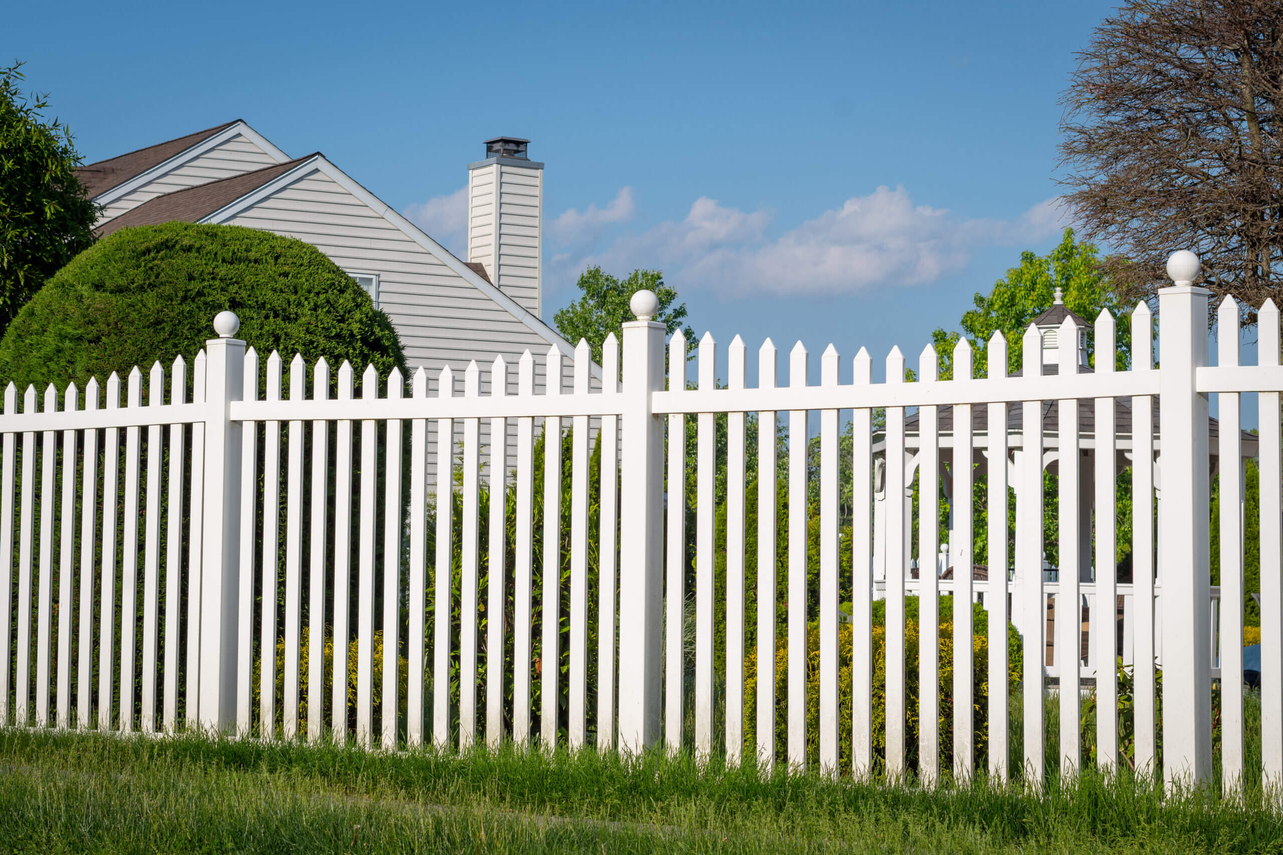 A white vinyl picket fence complementing a well-landscaped backyard