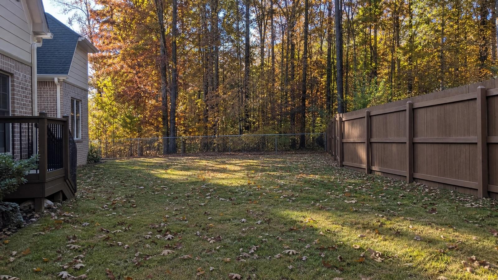 Brown vinyl privacy fence and a galvanized chain link section enclosing a wooded North Georgia back yard