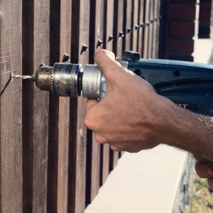 Man hands drilling wooden fence to metal construction.